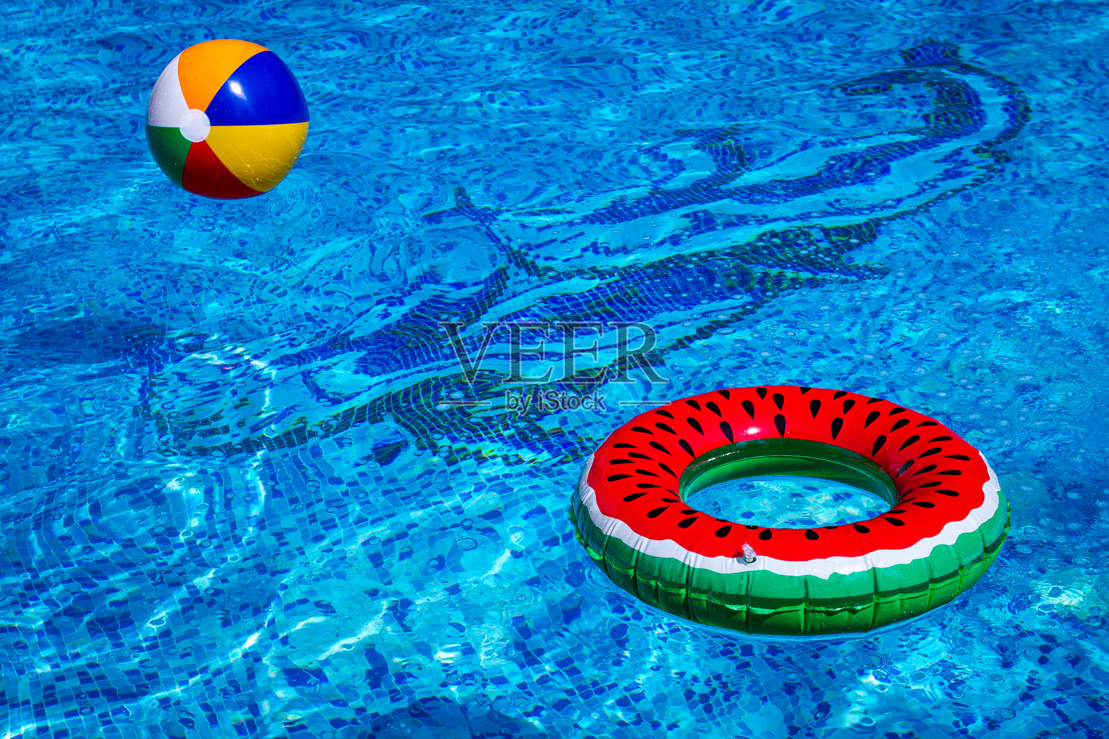 五颜六色的沙滩球和西瓜圈漂浮在泳池水面上，阳光明媚的夏日，没有人。照片摄影图片