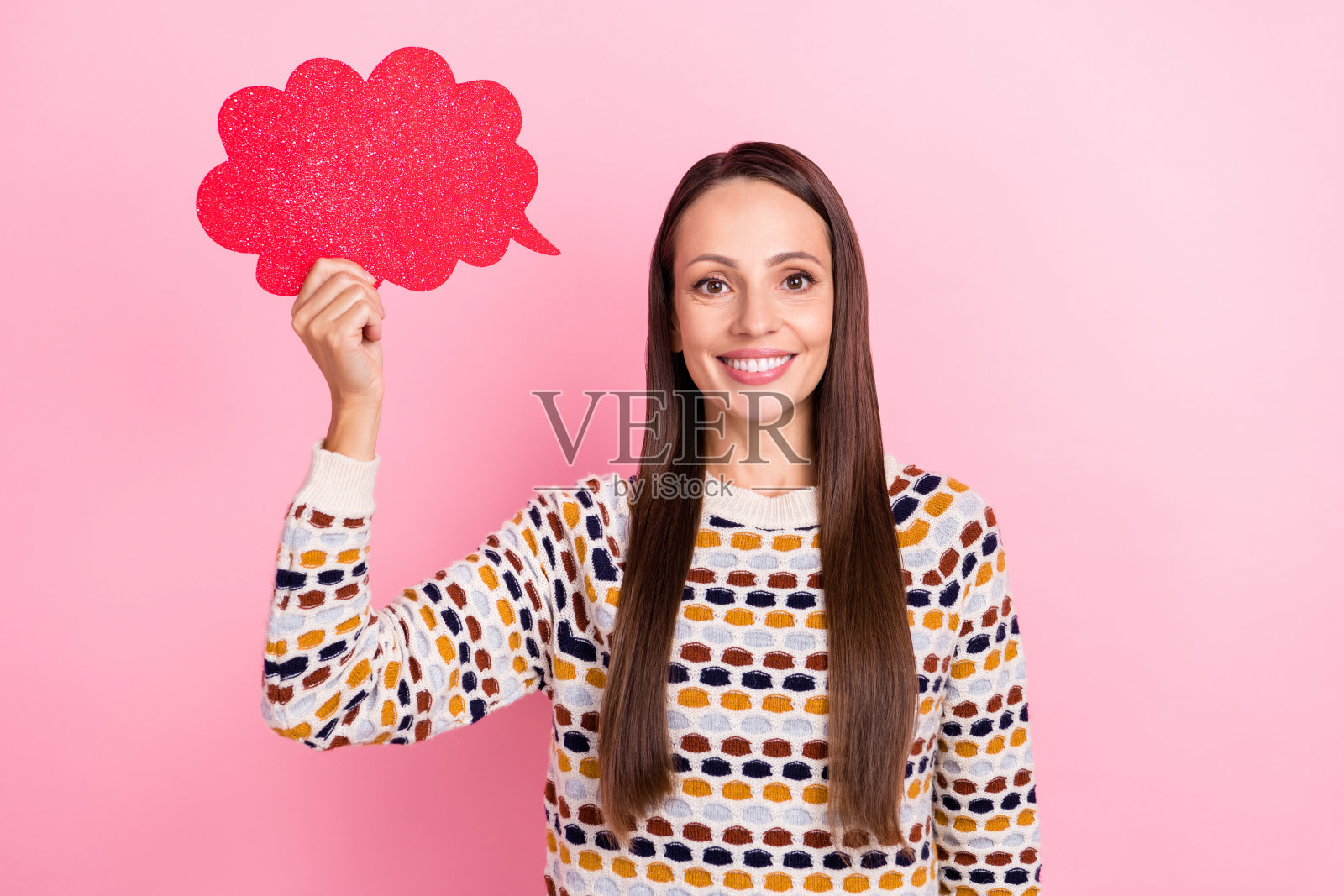 有趣可爱的成熟的女士穿着印花毛衣，手持空白对话框，微笑着，背景为粉色。照片摄影图片