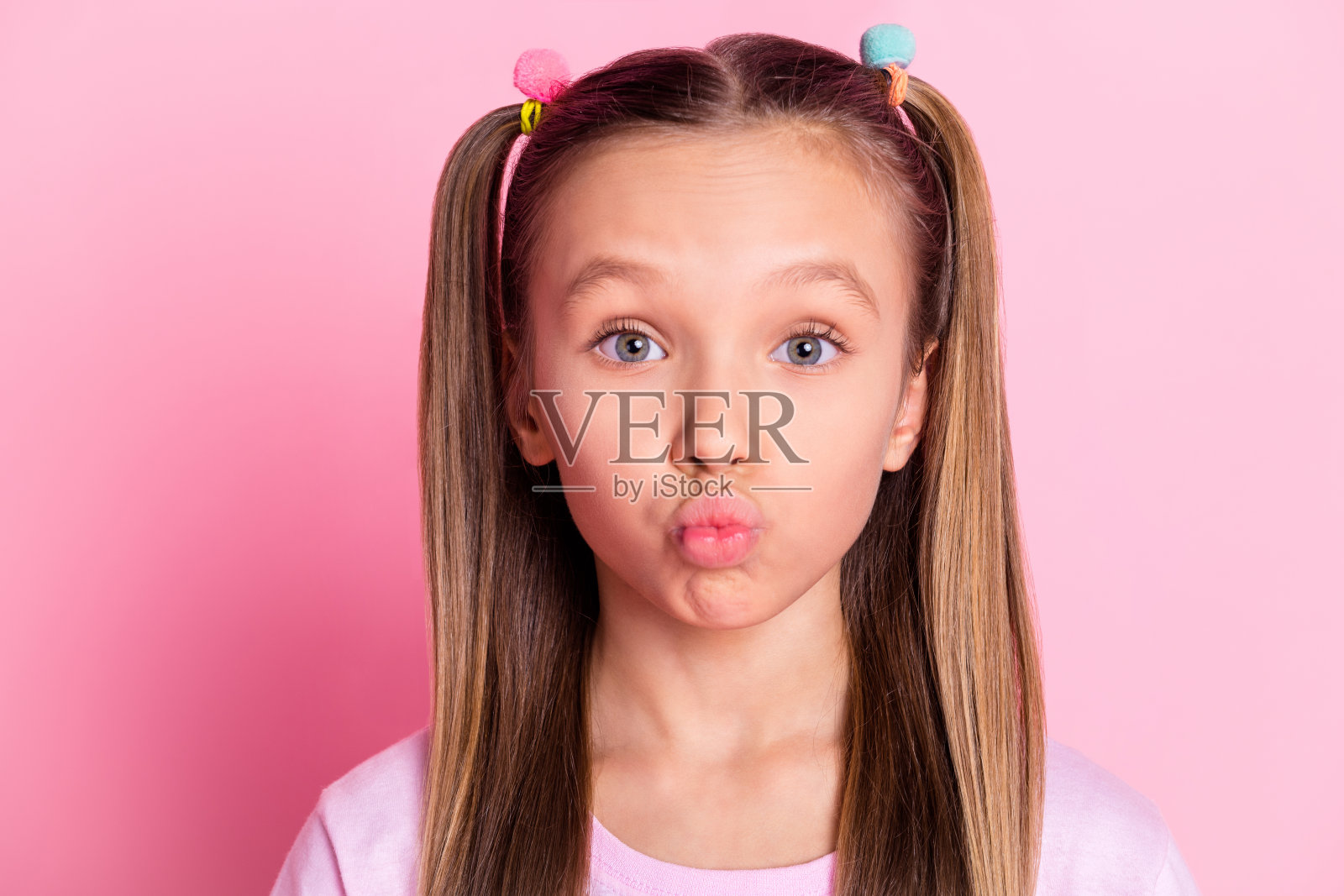 漂亮乐观的金发女孩在粉色背景上吹吻，穿着T恤。照片摄影图片