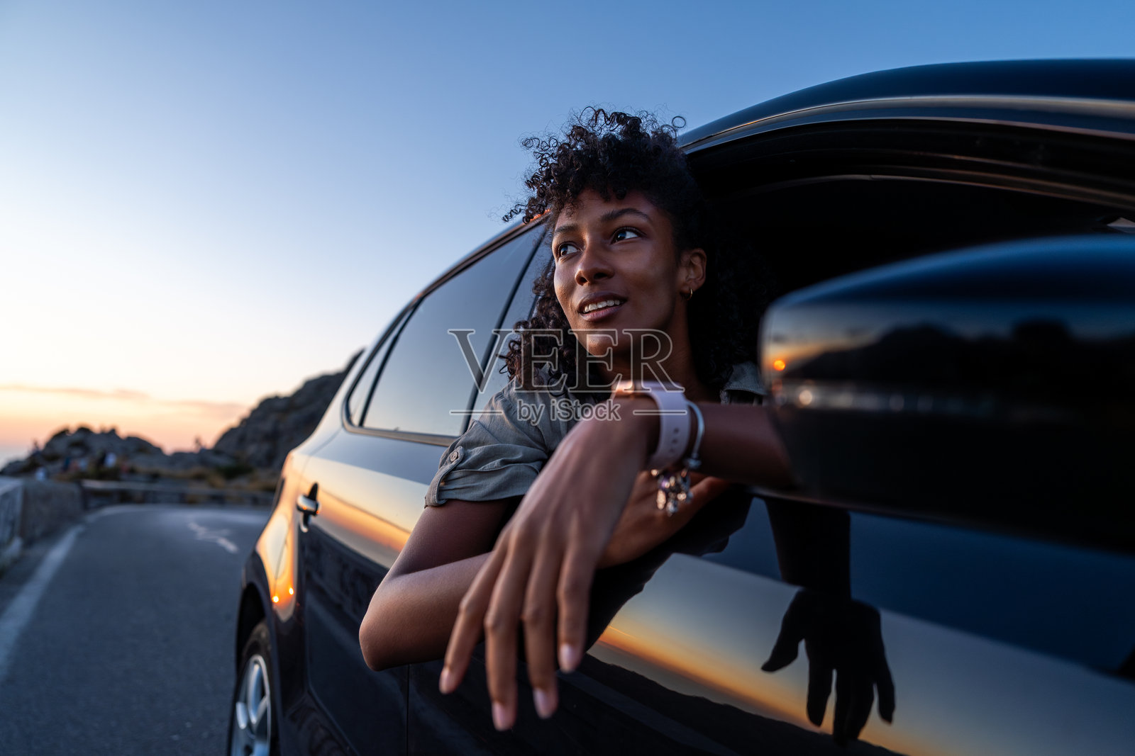 女人在日落时从车窗外探出身子照片摄影图片