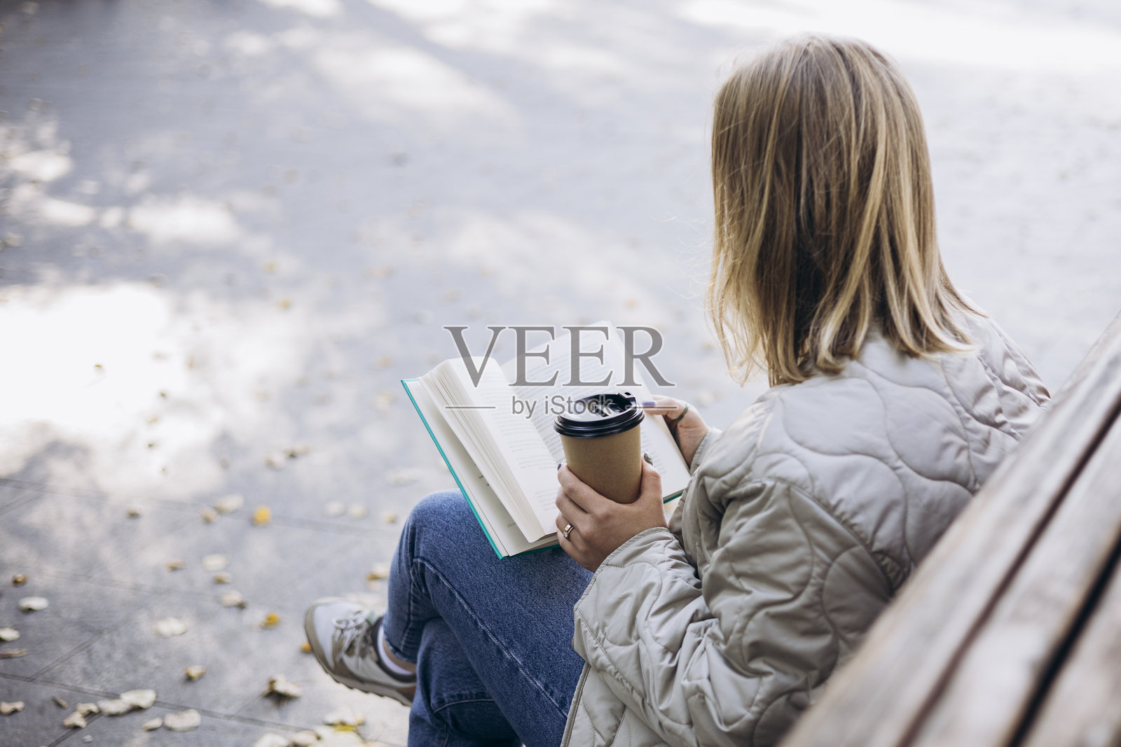 年轻女性在秋季公园的长椅上阅读书籍并喝咖啡。照片摄影图片