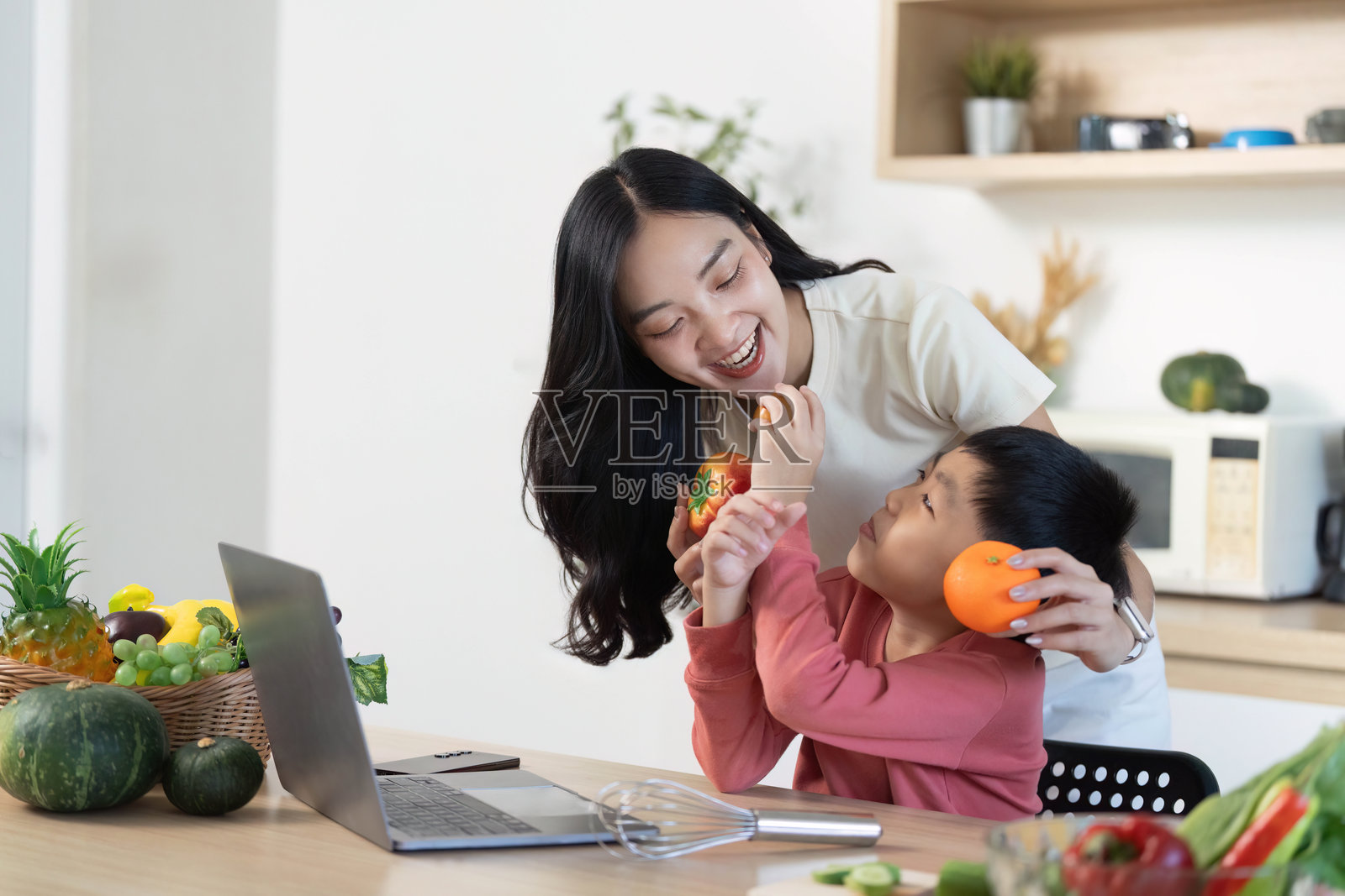 健康零食时间：母亲和儿子在快乐的厨房时光中分享橙子照片摄影图片