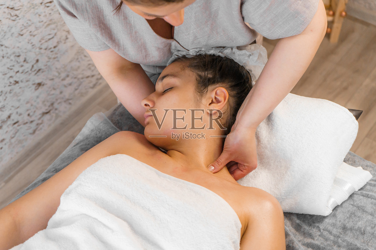 一位女性在桌子上接受颈部按摩。水疗、健康与放松的概念照片摄影图片