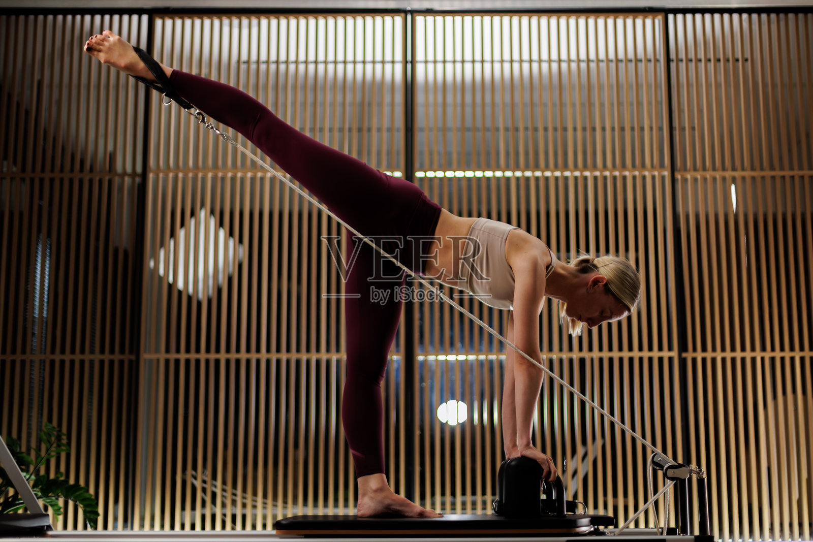 健身爱好者在现代工作室中进行拉伸练习，工作室内有木质装饰和温暖的灯光。照片摄影图片