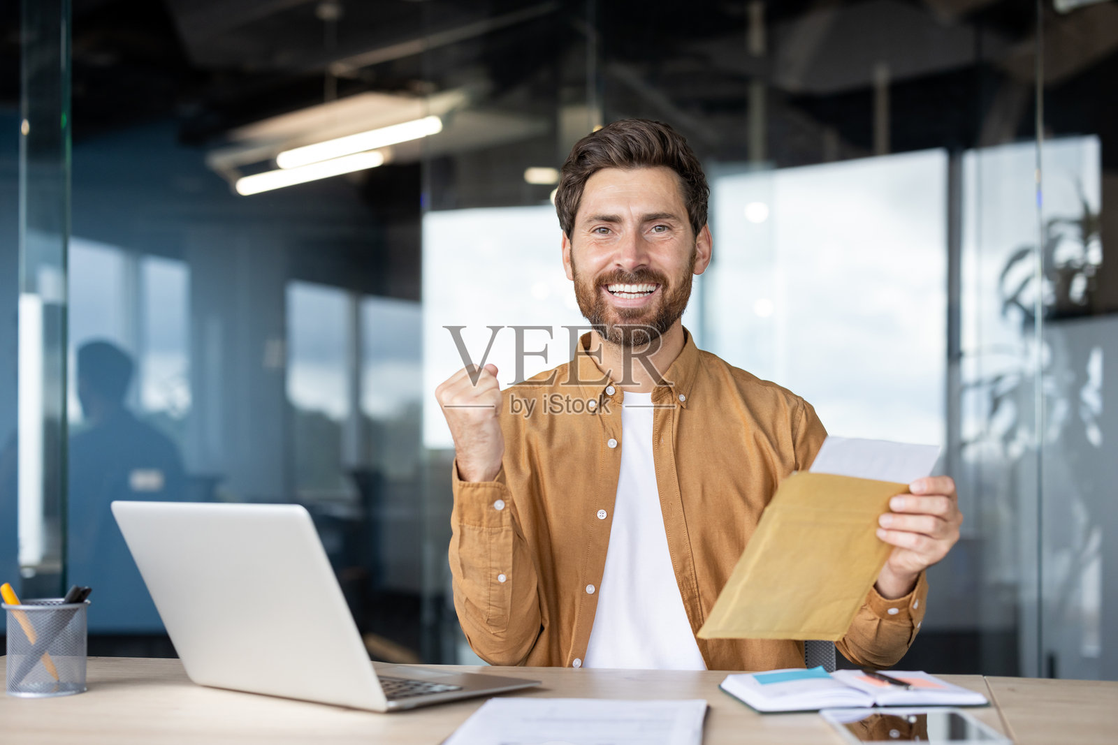 快乐的男人在现代办公室工作空间庆祝成功，手里拿着信封照片摄影图片