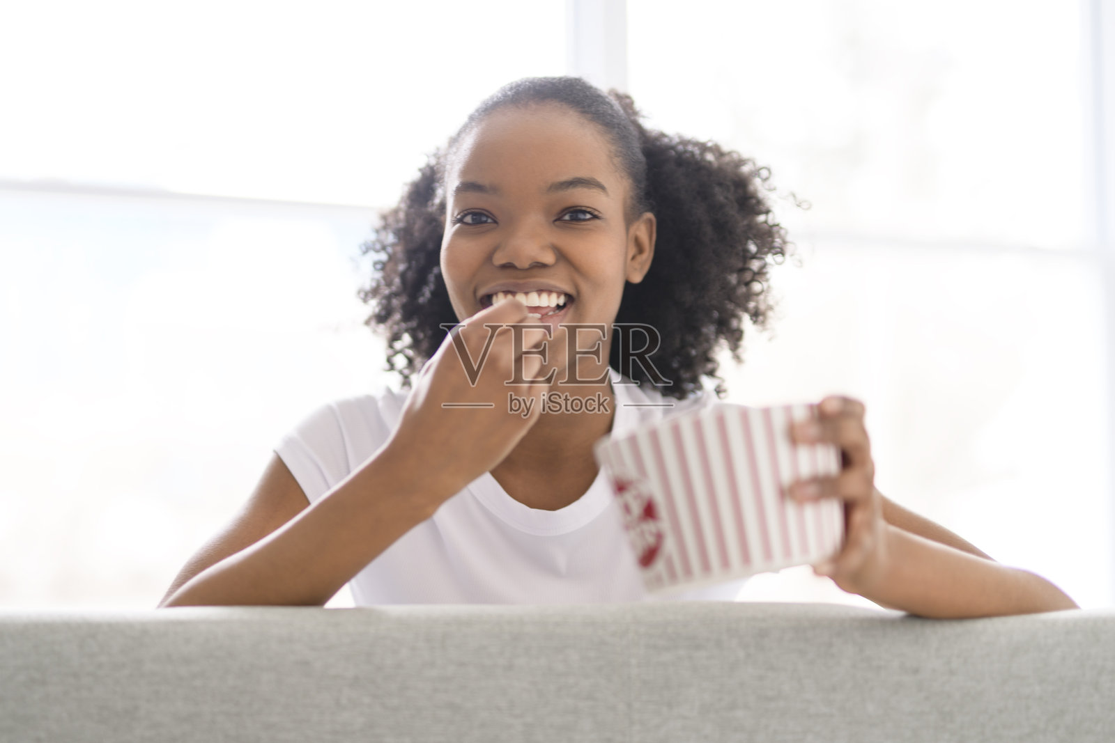 兴奋的美国青少年女孩在室内享受电影并吃爆米花。照片摄影图片