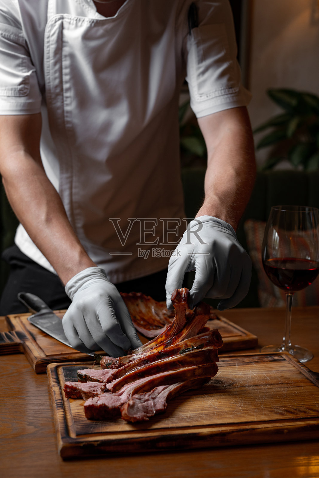 厨师在木板上切割多汁的烤猪肋排，特写镜头展示带骨的烤肉，餐厅厨房的食物准备。照片摄影图片