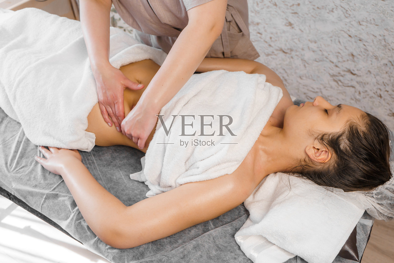 苗条年轻女性在水疗沙龙接受腹部按摩。照片摄影图片