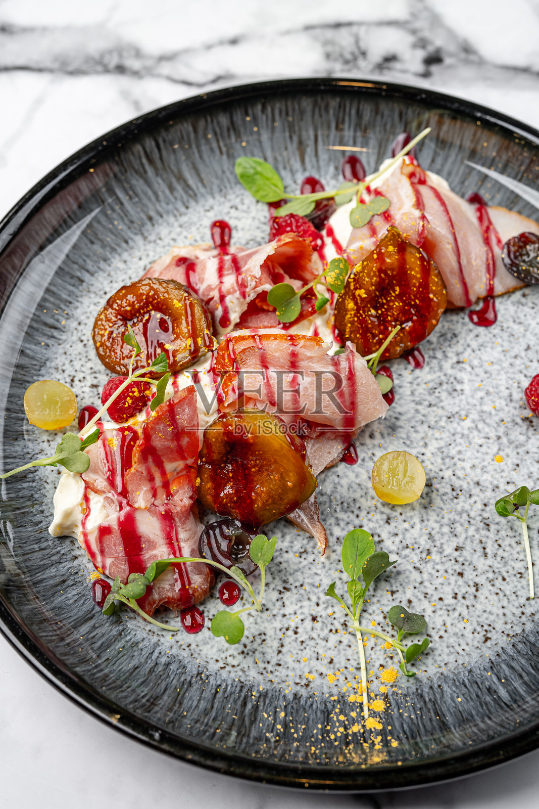 美味的意大利火腿配烤无花果、奶油奶酪、新鲜葡萄、覆盆子酱和微型绿叶，盛放在现代黑色陶瓷盘上照片摄影图片