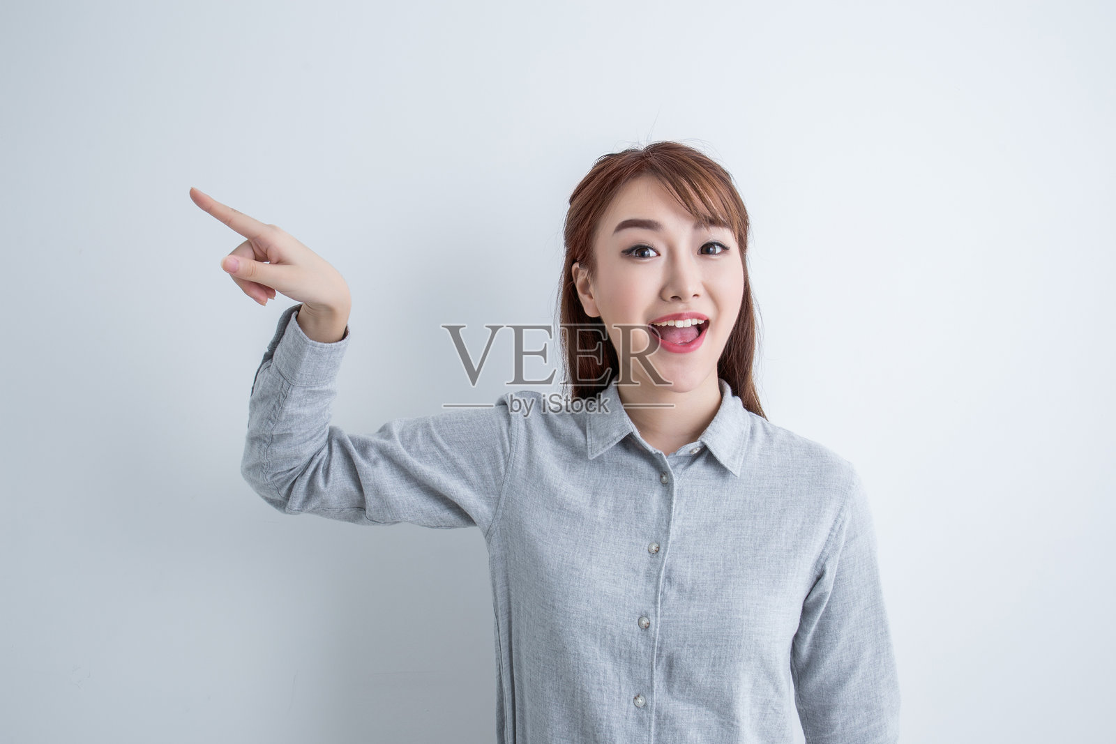 年轻女性穿着休闲衬衫，兴奋地指着某处。照片摄影图片