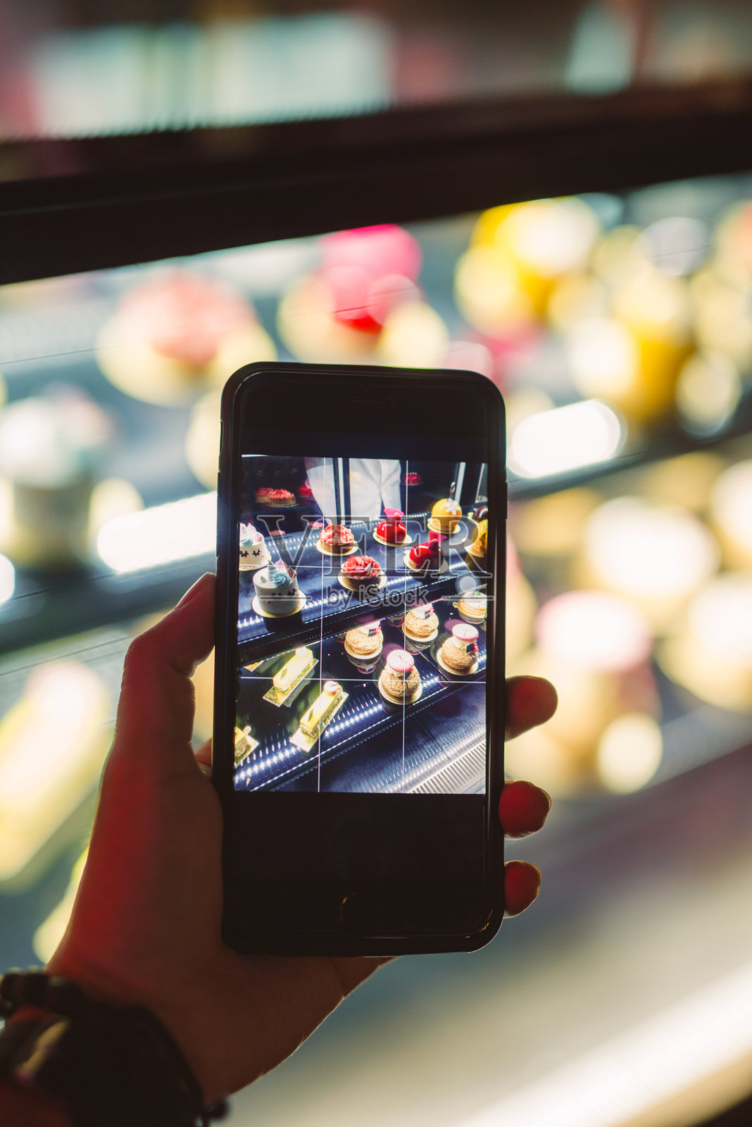 手持智能手机拍摄展示柜中的甜点照片摄影图片