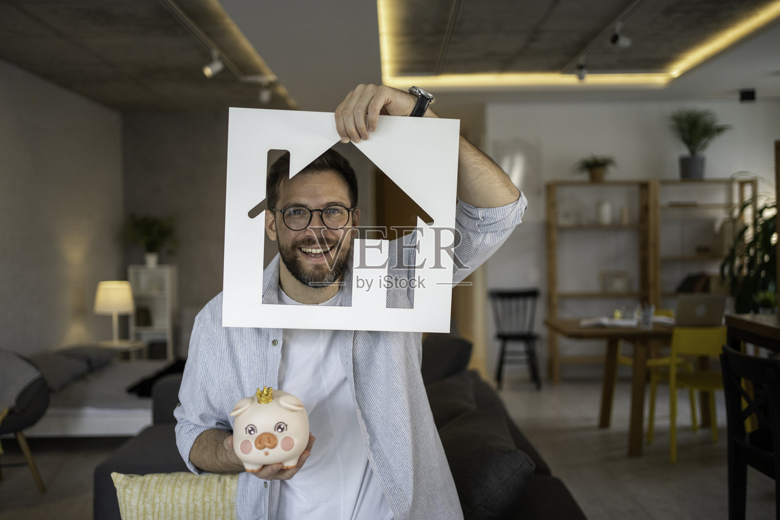 男人手持房屋形状和储蓄罐，为购房储蓄照片摄影图片