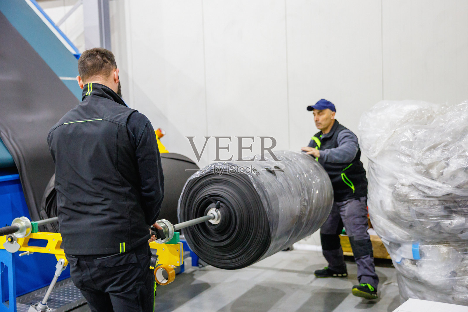 两名工人在工业设施中处理大型卷材的输送系统照片摄影图片