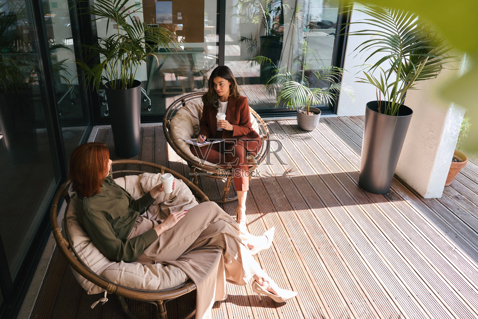 两位忙碌的女商人在阳光明媚的绿色办公室里交谈工作。俯视图。照片摄影图片