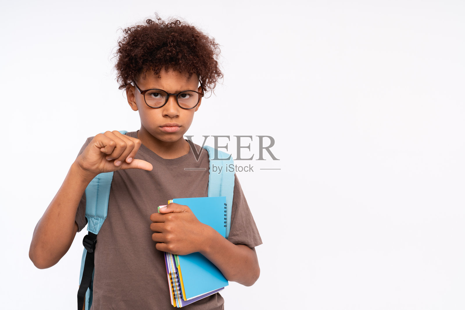 伤心的非裔美国小男孩，手持作业本，孤立在白色背景前，做出不喜欢的手势，竖起大拇指向下。表示不同意的概念，留有空白空间。我不喜欢它！照片摄影图片