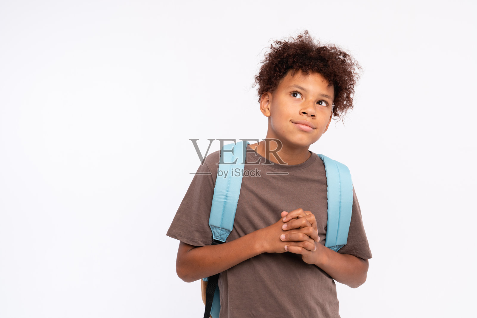 思考的非裔美国小男孩站在背景前，双手交叉，仰望着，脸上带着梦幻般的顽皮表情，充满想象力，留有空白空间。照片摄影图片