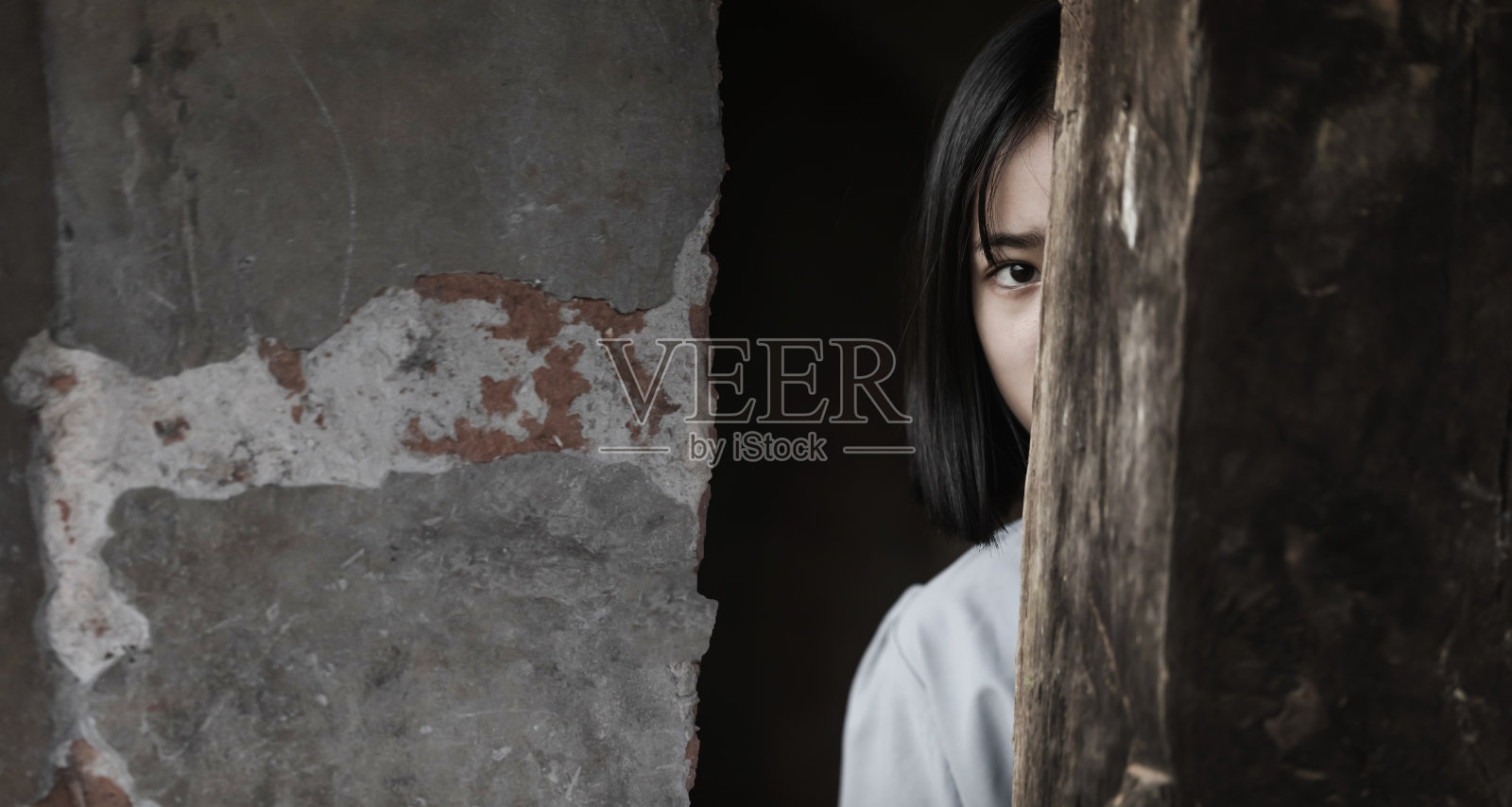害怕的年轻少女从阴暗的旧房间里窥视。针对儿童和女性的暴力。照片摄影图片
