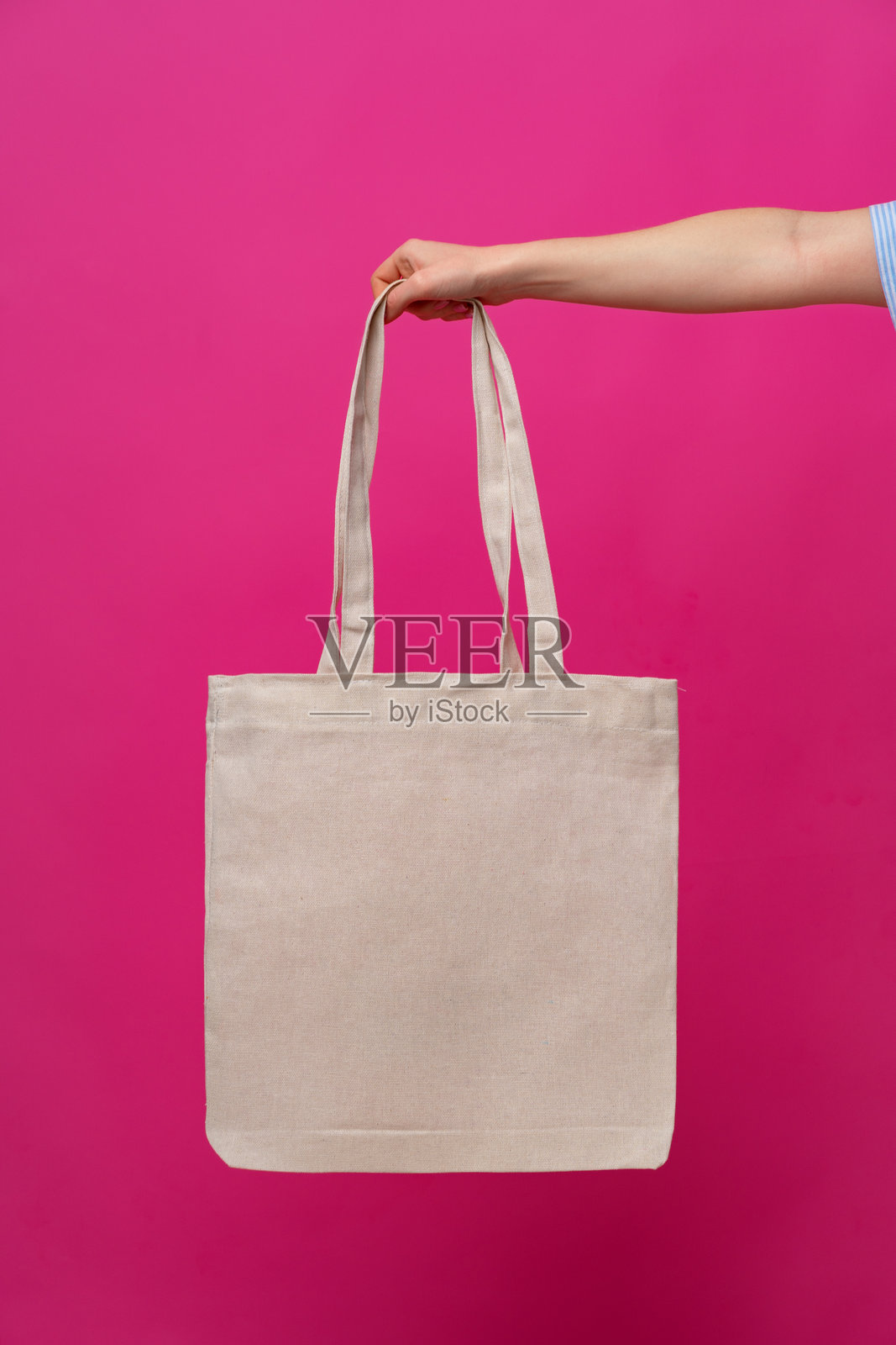 女性手持环保或可重复使用的购物袋，背景为粉色。照片摄影图片