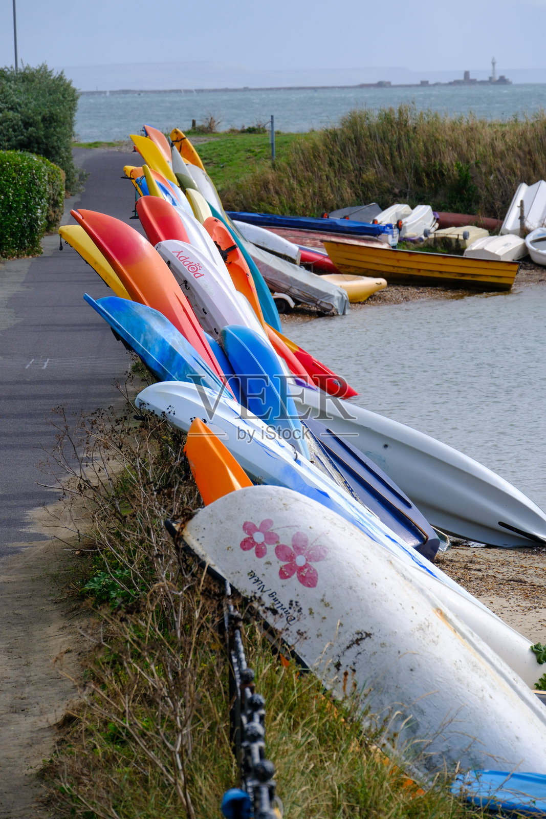 英格兰南部住宅旁的海滩上,整齐排列的皮划艇、独木舟、立式划水板和小船。照片摄影图片