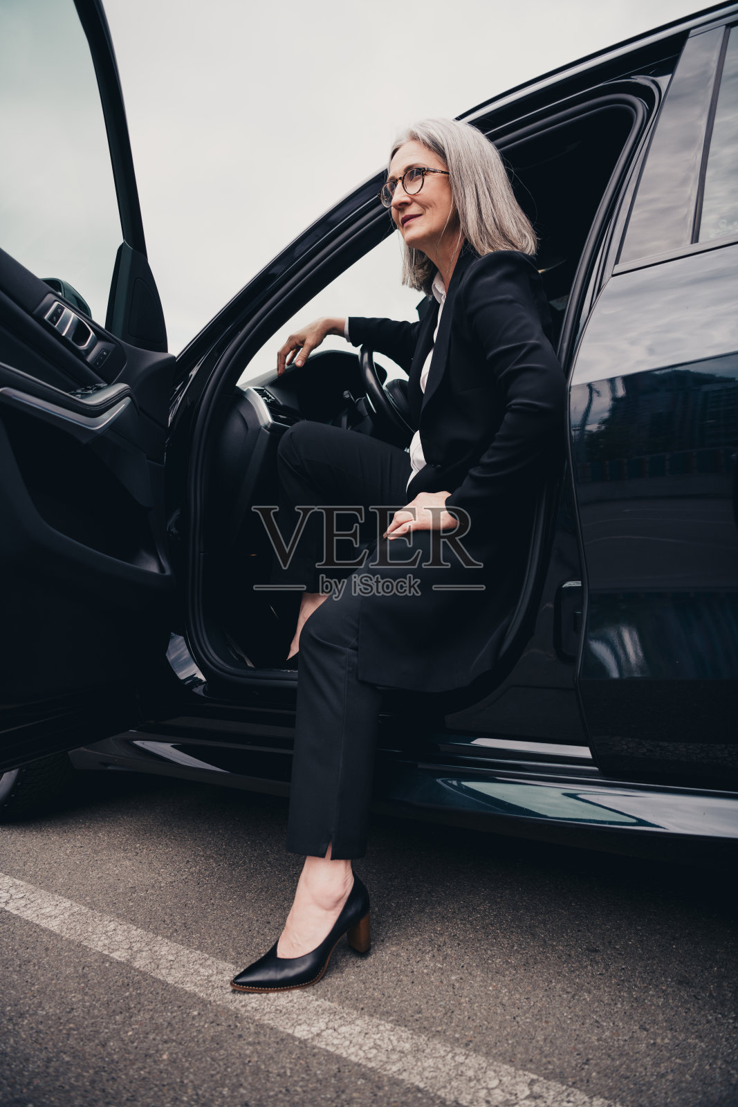 成功的成熟的女商人在繁忙的城市街道上穿着优雅的服装走出汽车照片摄影图片