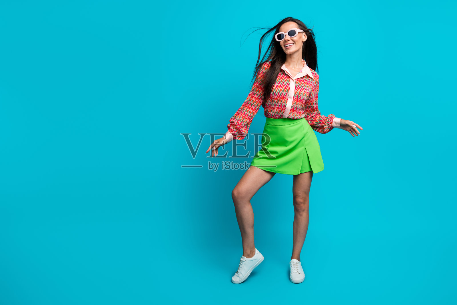 全身照，穿着夏季服装、戴着太阳镜的可爱搞笑拉丁裔女士在愉快的心情中跳舞，背景为蓝绿色。照片摄影图片