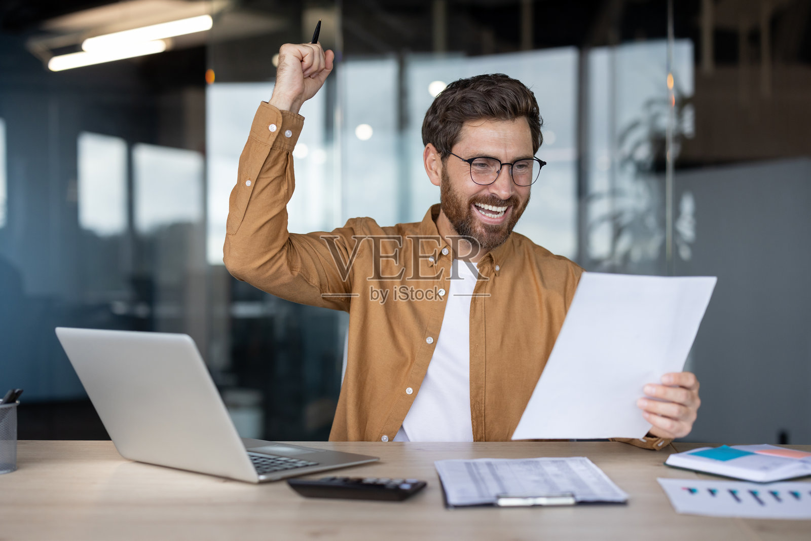 兴奋的商人在办公桌前庆祝成功，手中拿着文件照片摄影图片