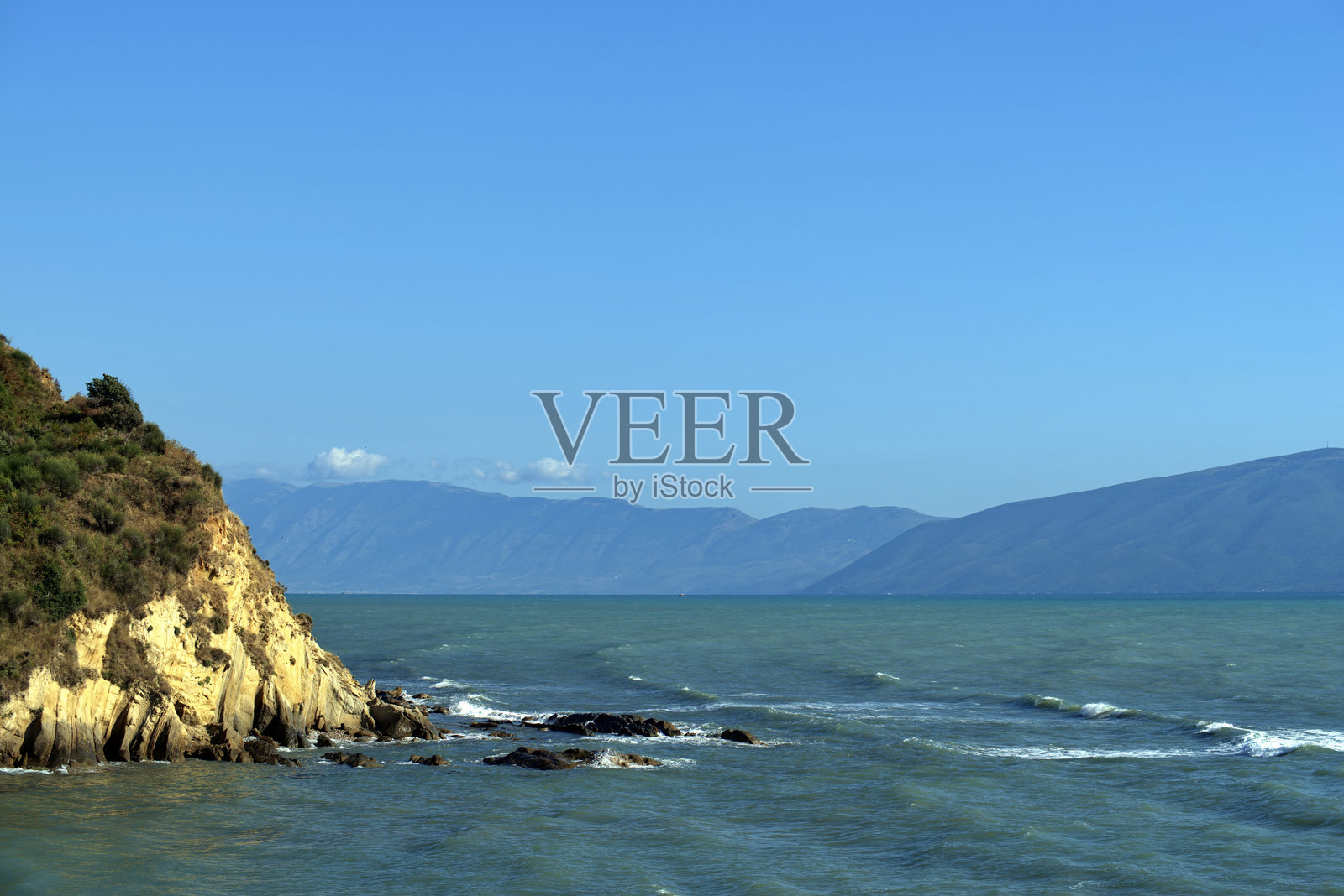 海岸悬崖在波涛汹涌的海面上与山脉和天空相映成趣照片摄影图片