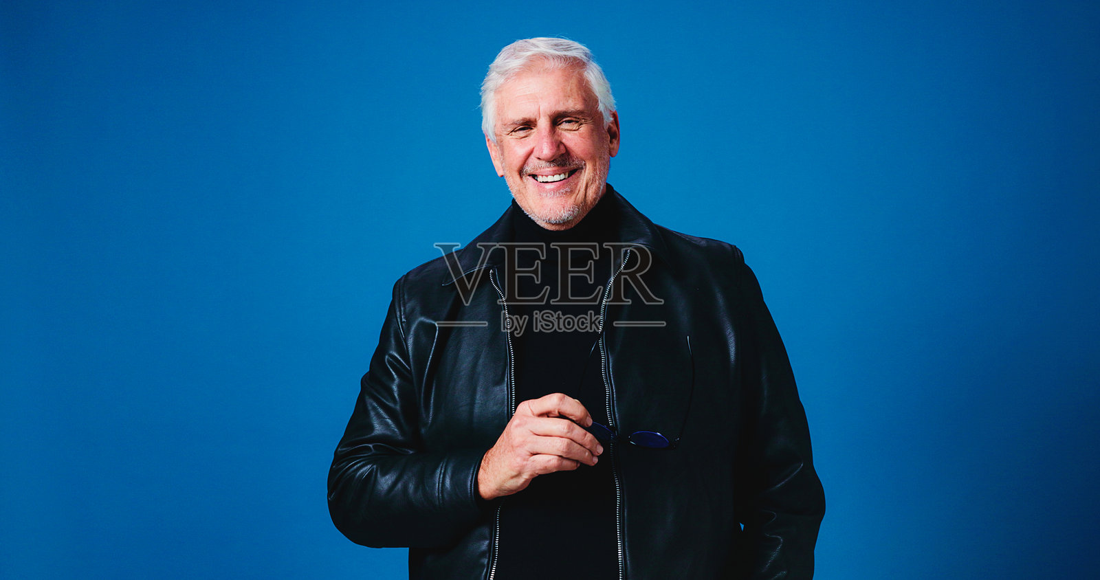 肖像，微笑的男人在工作室，时尚与自信的太阳镜，蓝色背景。退休人员，成熟的人戴着墨镜，穿着时尚的衣服和皮夹克，充满自豪感和眼镜。照片摄影图片