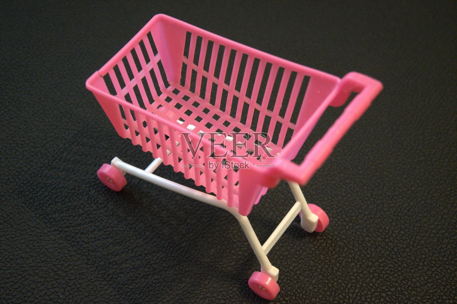粉色迷你购物车放在黑色皮革背景上照片摄影图片