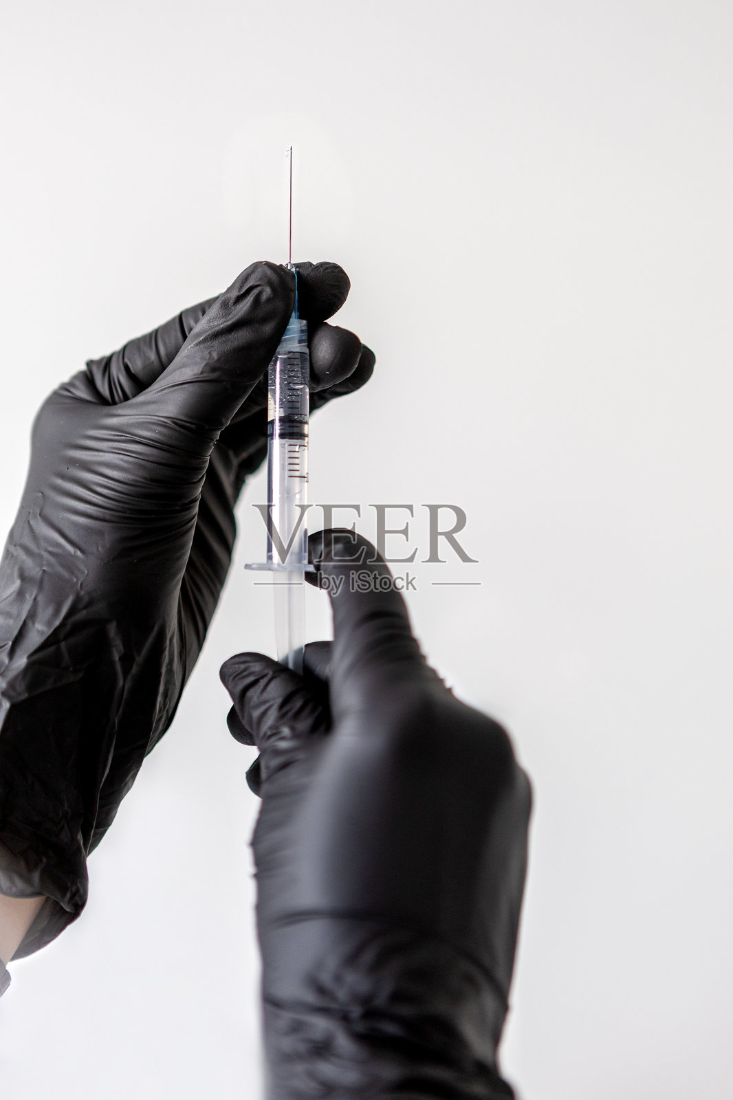 医生戴着黑色手套的手握着注射器，准备在白色背景下进行疫苗接种、美容或医疗治疗。照片摄影图片