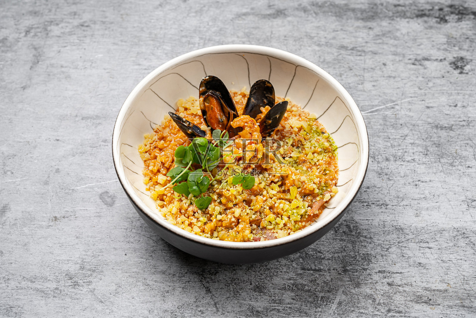 海鲜烩饭，配有贻贝、虾、帕尔马干酪和新鲜香草，盛放在陶瓷碗中，背景为灰色石材，传统意大利美食照片摄影图片