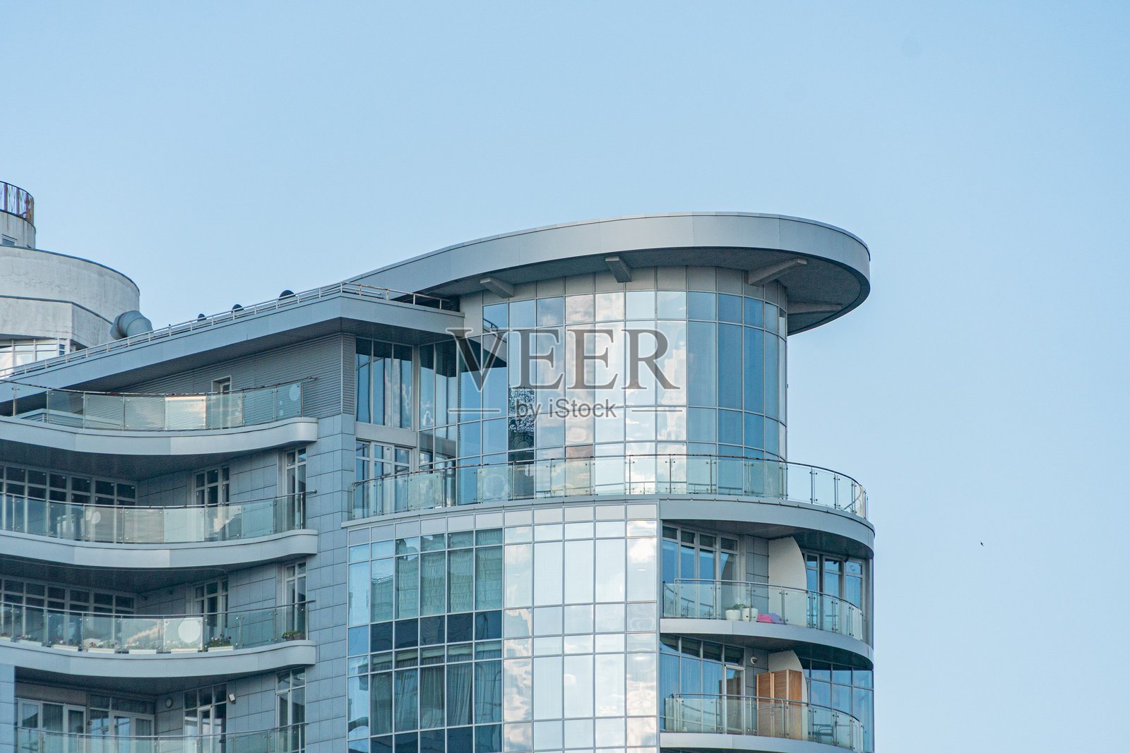 现代住宅建筑，圆润的边缘，蓝灰色外立面和大型反射玻璃窗，部分窗户上装有白色金属阳台，阴云密布的天空，宁静的氛围，写实风格照片摄影图片