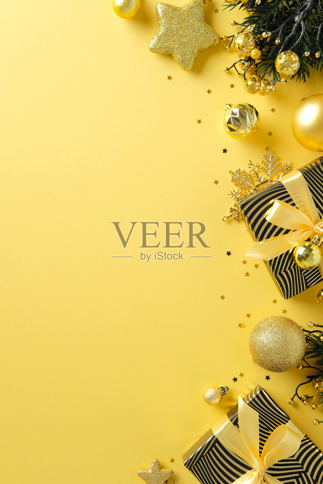 时尚的圣诞扁平布局，金色装饰品、条纹礼物和松枝在黄色背景上。照片摄影图片