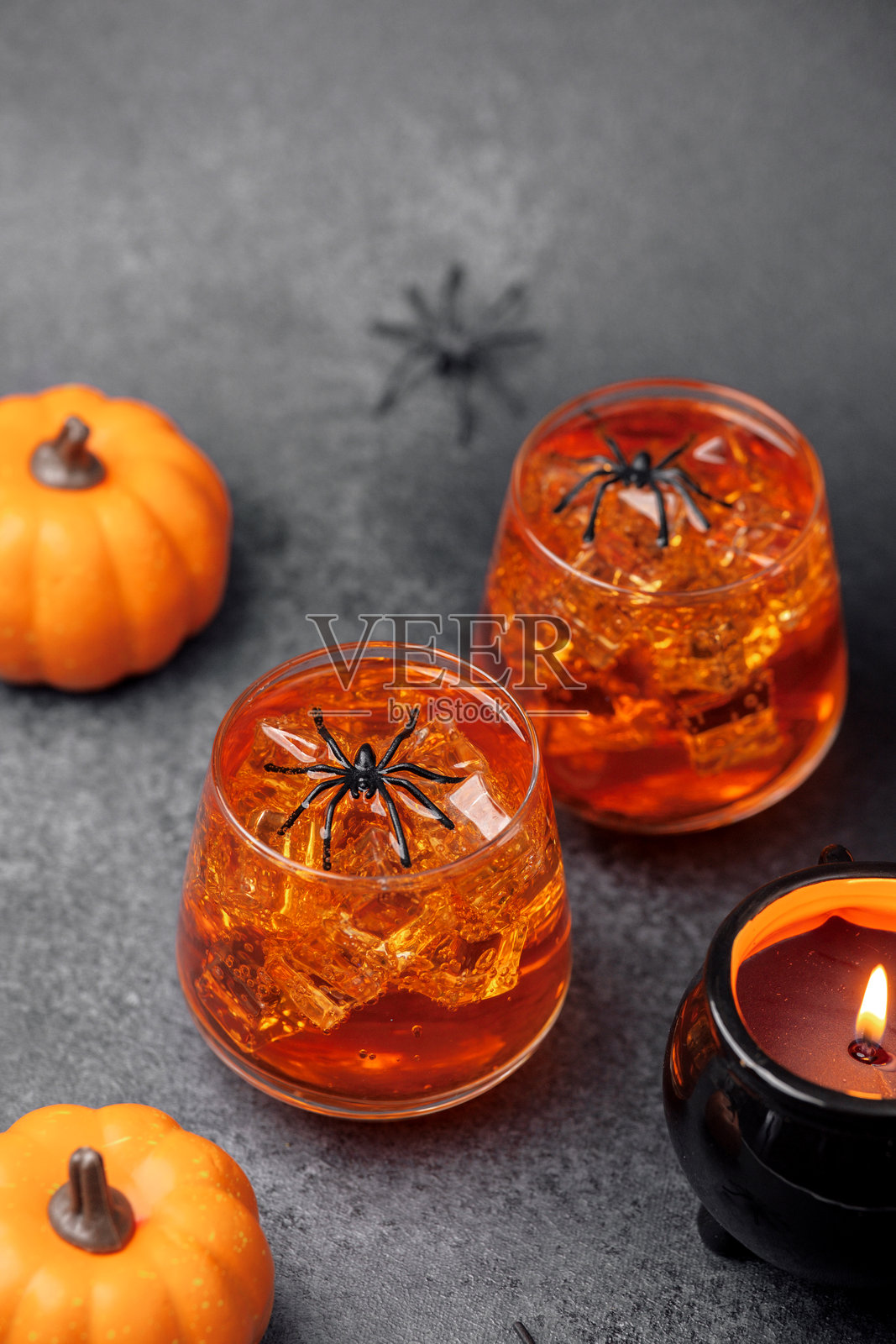 万圣节橙色饮料，配有冰块、玩具蜘蛛、南瓜和锅炉蜡烛照片摄影图片