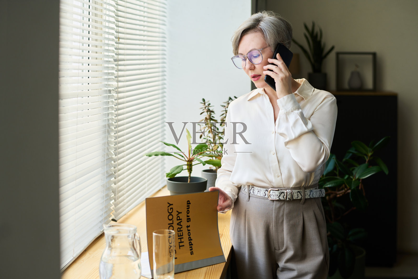 资深女性心理学家在窗边进行电话咨询照片摄影图片