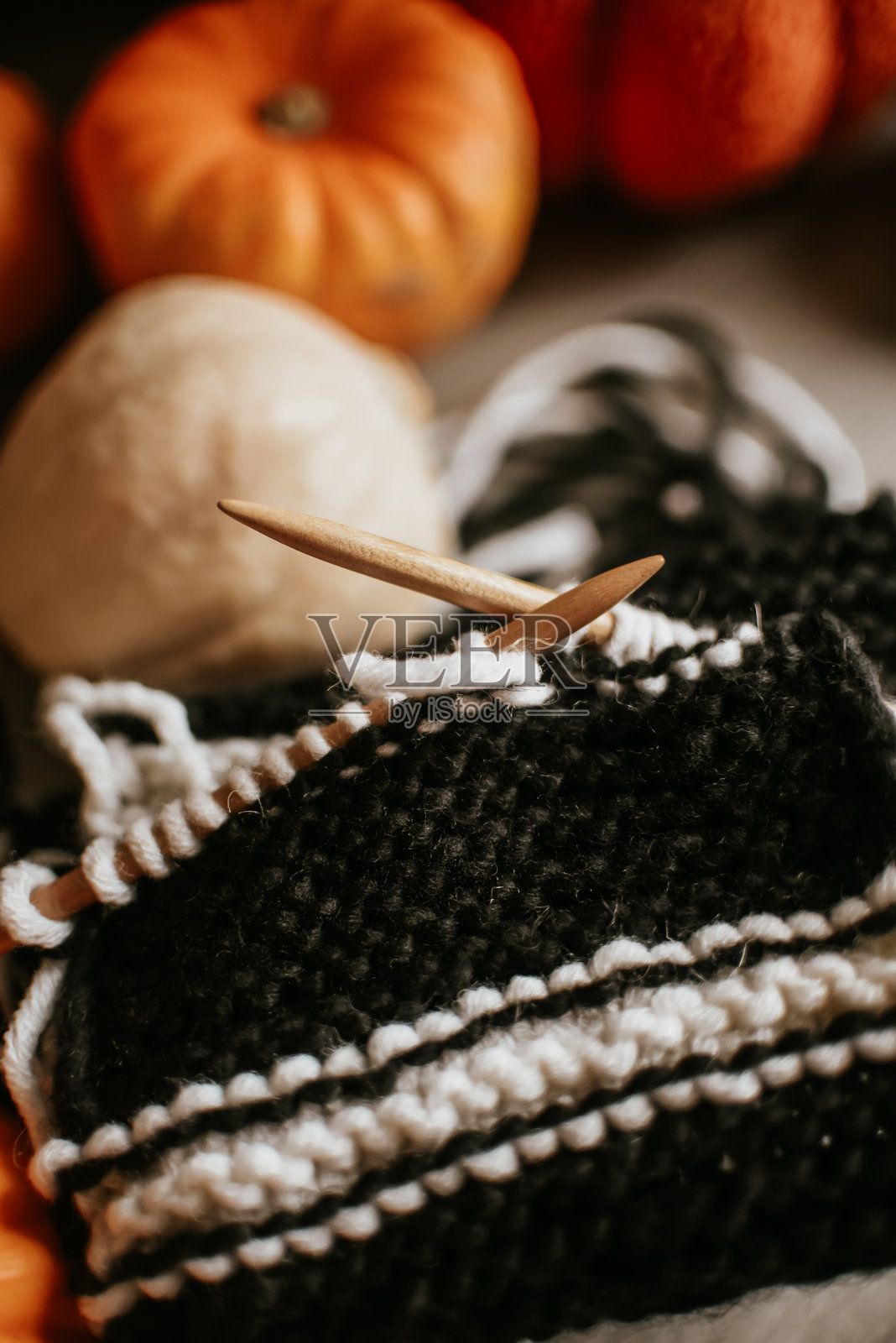 黑白毛线在木针上的编织项目特写，背景中有南瓜，营造出温馨的秋季氛围照片摄影图片