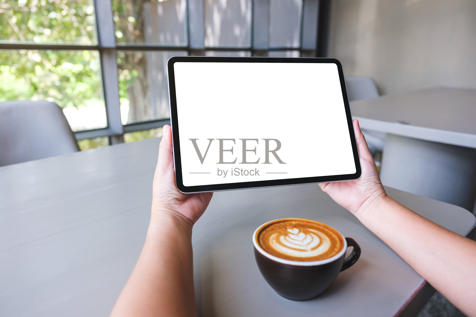 女性在咖啡馆里手持数字平板，屏幕上是空白的白色桌面。照片摄影图片