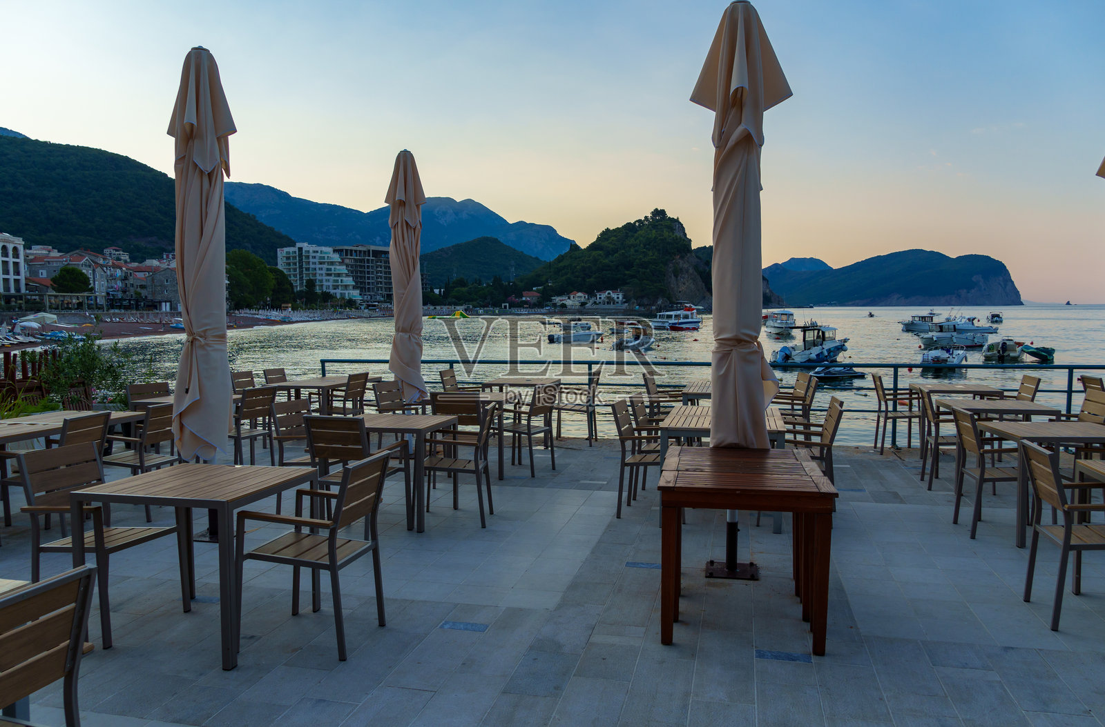 亚得里亚海岸的日出，黑山佩特罗瓦茨市滨水区的街头咖啡馆，清晨，海岸线，桌子和伞，太阳在山上升起照片摄影图片