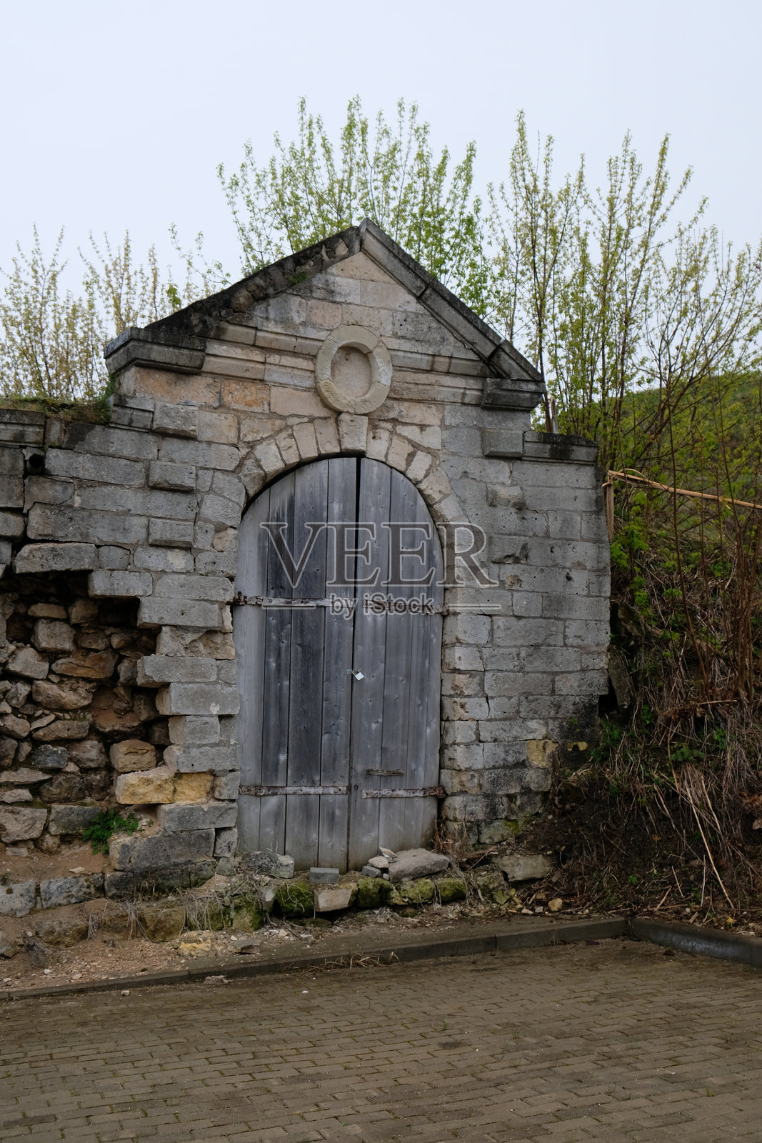 古老的石头建筑，木门嵌在阴云密布的绿色山坡中照片摄影图片