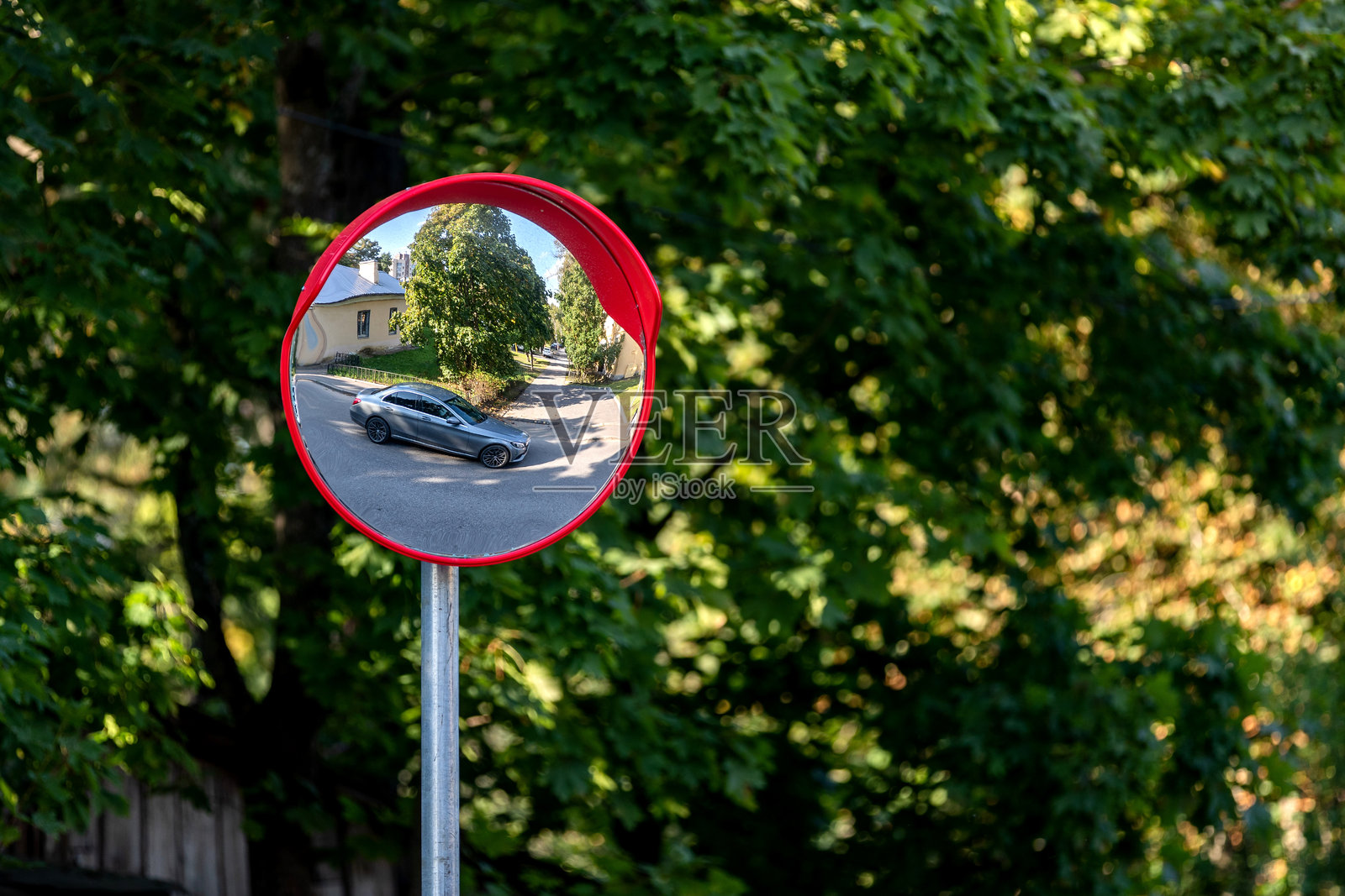 一个圆形的道路安全镜子反射出一辆白色汽车，背景是树木。照片摄影图片