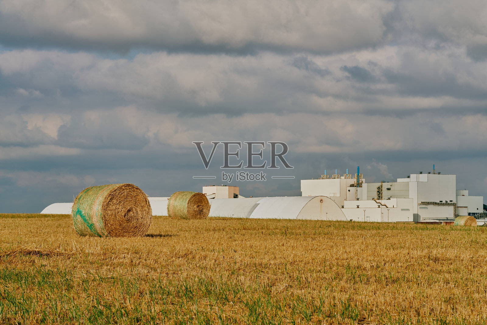 萨斯喀彻温省农田上的干草 bale 和工业建筑照片摄影图片