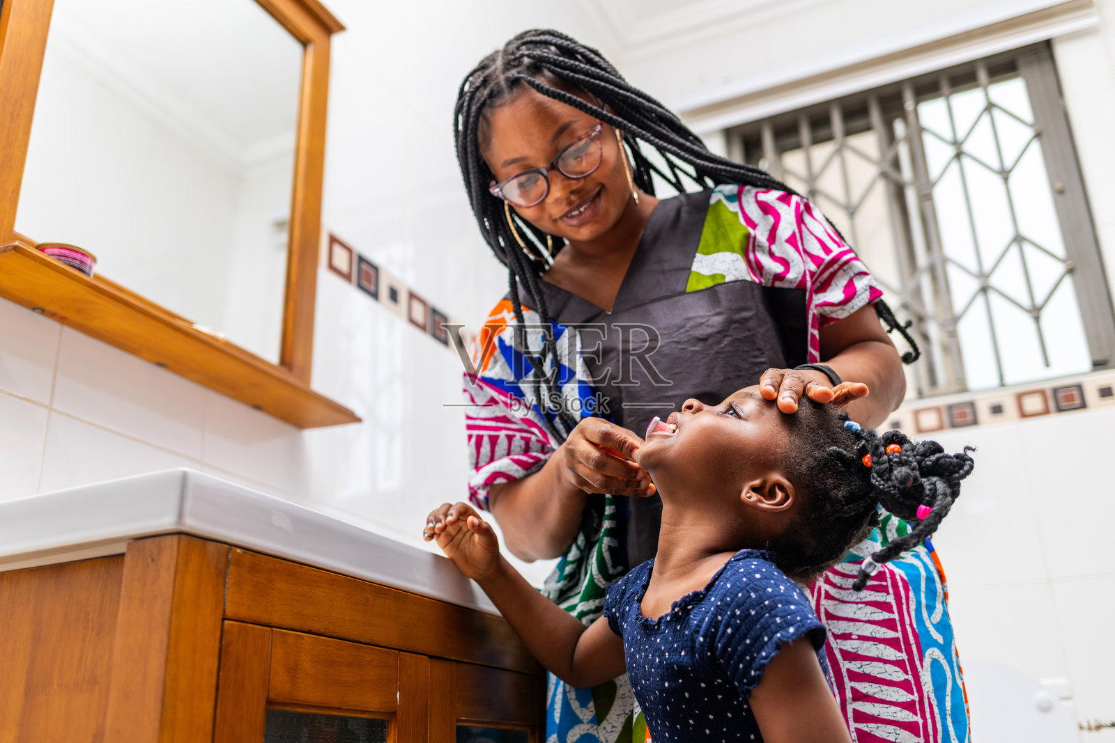 日常口腔卫生习惯。非洲母亲在家中的浴室里帮助小女儿刷牙。照片摄影图片