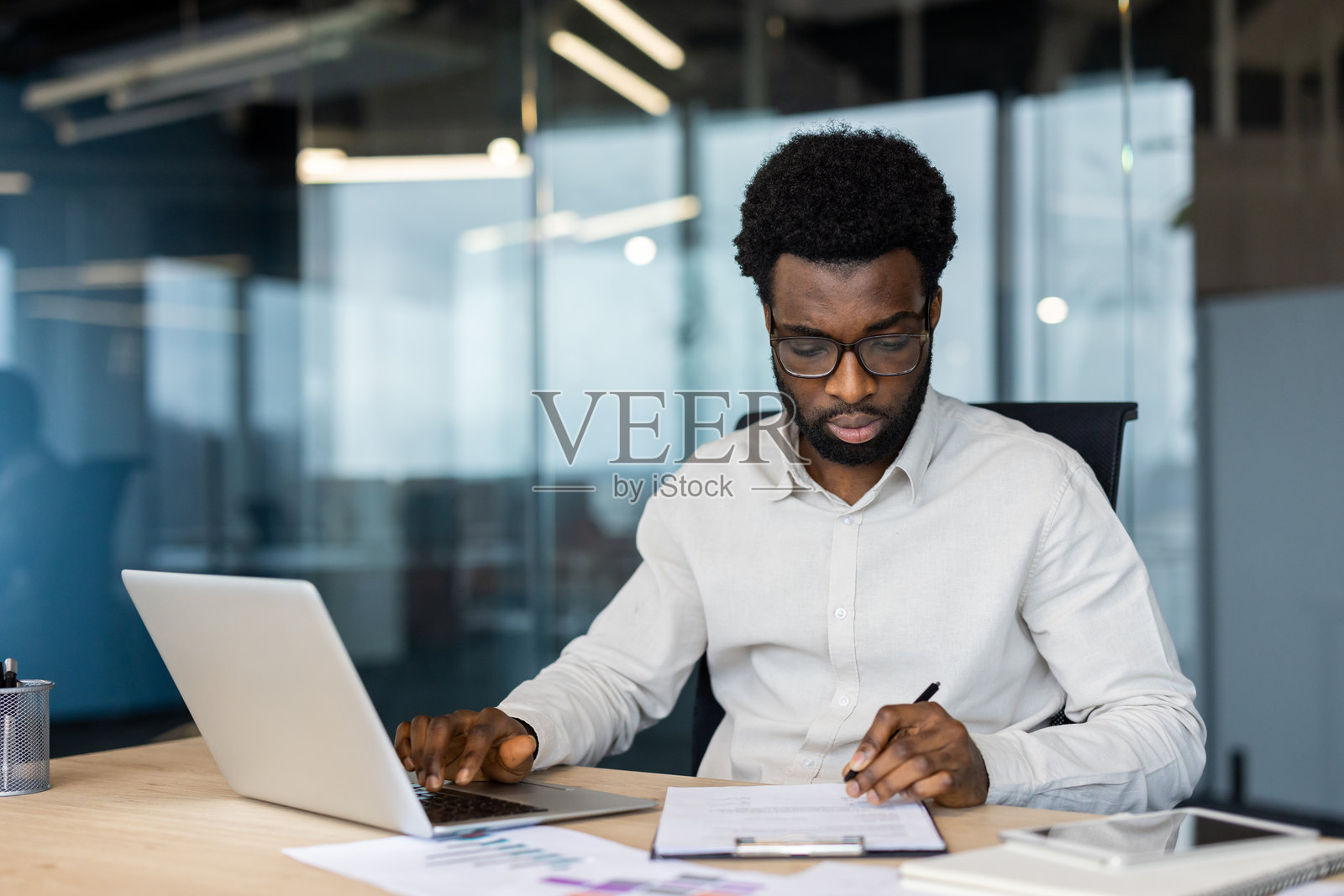 专注的黑人商人在现代办公室中使用笔记本电脑和文件工作照片摄影图片