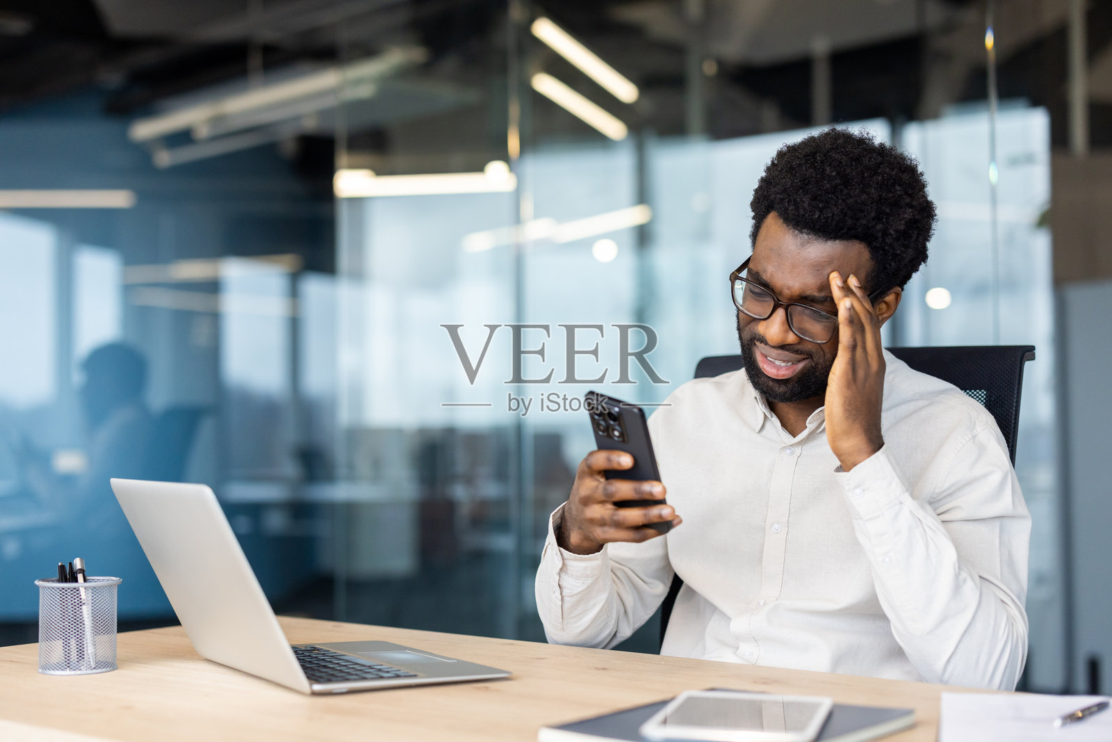 商人在现代办公室桌前使用智能手机时感到压力照片摄影图片