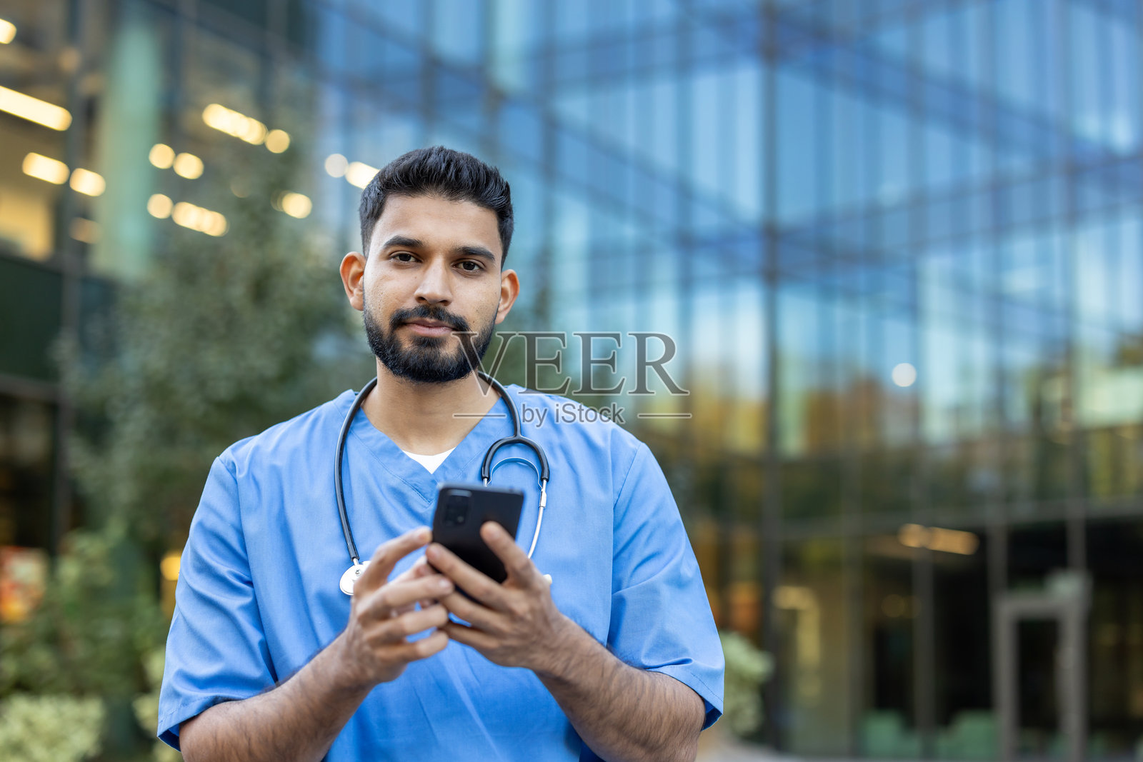 一位穿着医务工作服的医生在建筑外使用智能手机。照片摄影图片