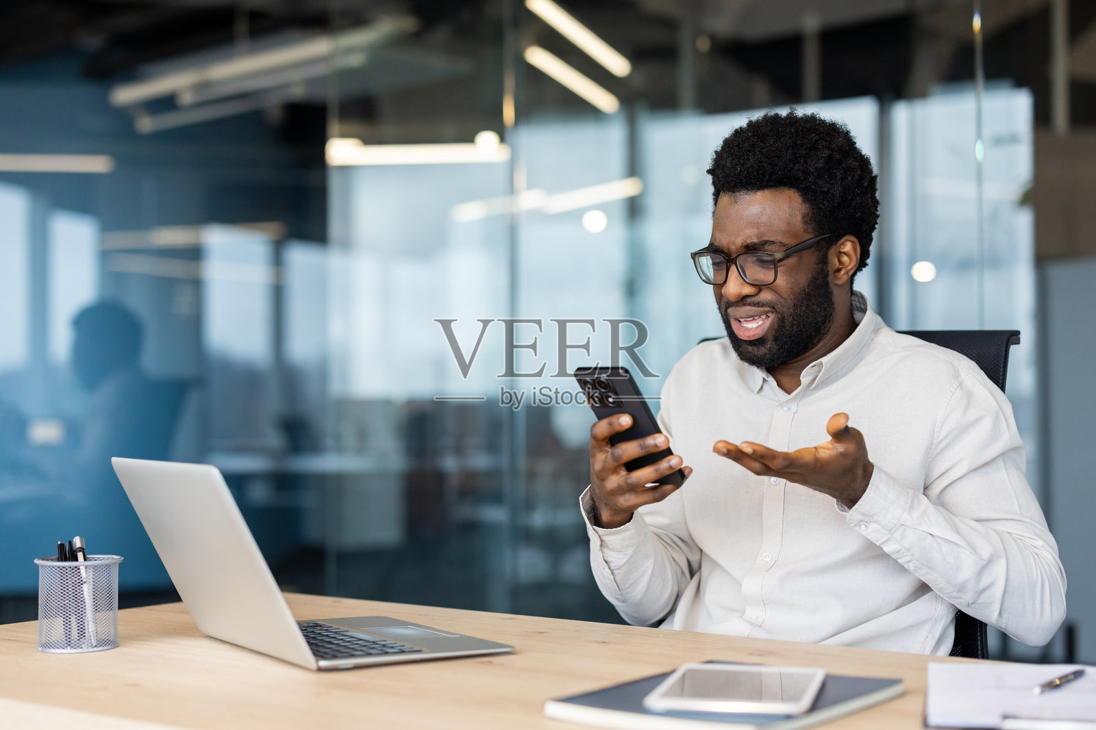 一位忧虑的非裔美国男性在办公室查看手机信息。照片摄影图片