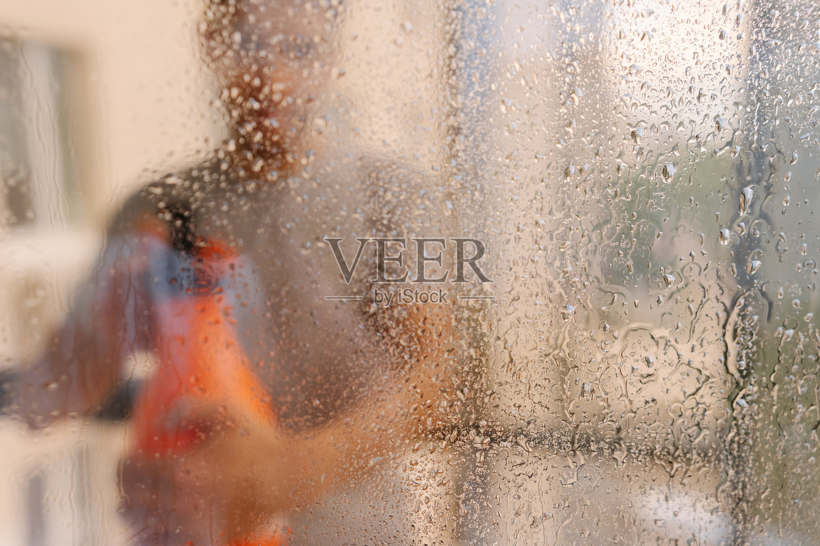 模糊的男管家肖像，喷洒窗户清洁剂，玻璃表面点缀着水滴，营造出柔焦效果，强调工作场所的清洁过程。照片摄影图片