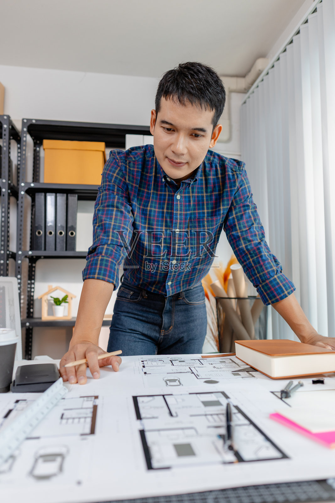 年轻建筑师在办公室中研究建筑模型和楼层平面图，分析细节并创造创新设计概念，展现出在建筑项目中的创造力、专注力和奉献精神。照片摄影图片