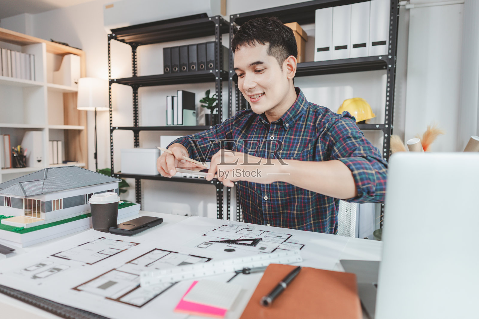 年轻男性建筑师在办公室桌前工作，绘制施工图纸并使用绘图工具，专注于建筑设计，展现出在建筑领域的创造力和奉献精神。照片摄影图片
