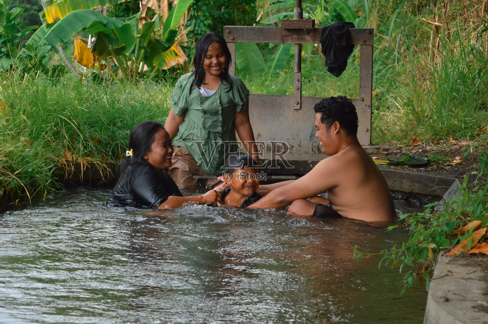 儿子自豪地站在父母之间，三人手牵手在灌溉小溪中。照片摄影图片